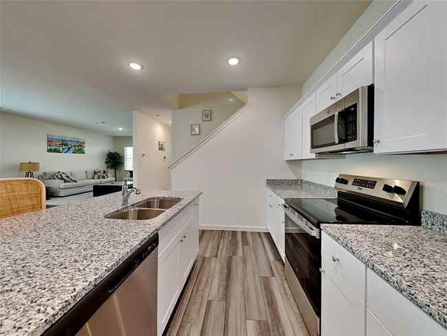 Kitchen with stainless steel appliances, light wood finished floors, white cabinets, light stone countertops, and recessed lighting | Image 4