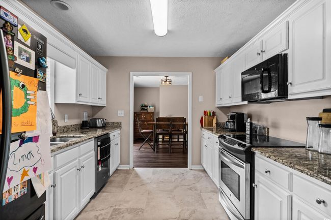 Kitchen featuring black microwave, freestanding refrigerator, stainless steel range with electric cooktop, white cabinetry, and dishwasher | Image 6