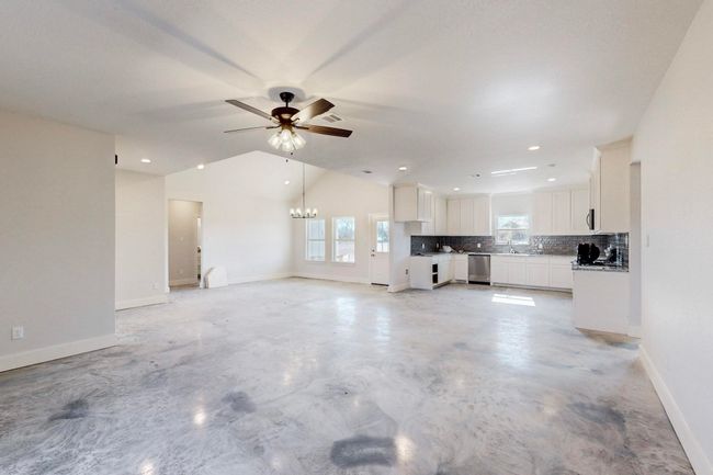 Unfurnished living room with ceiling fan with notable chandelier, concrete flooring, baseboards, and visible vents | Image 13