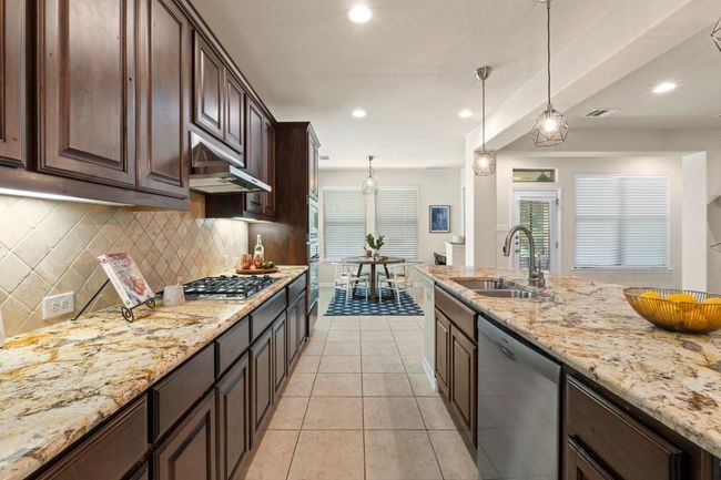 Kitchen featuring appliances with stainless steel finishes, backsplash, light stone counters, light tile patterned floors, and dark brown cabinetry | Image 11
