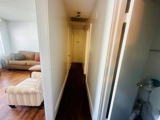 Hallway featuring attic access, a textured ceiling, wood finished floors, and baseboards | Image 7