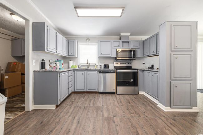 Kitchen featuring appliances with stainless steel finishes, gray cabinetry, ornamental molding, and light wood finished floors | Image 13