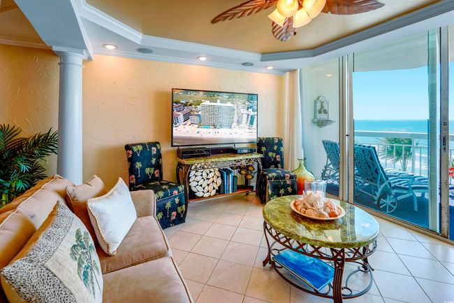 Tiled living room featuring ornamental molding, a raised ceiling, a textured wall, decorative columns, and ceiling fan | Image 9