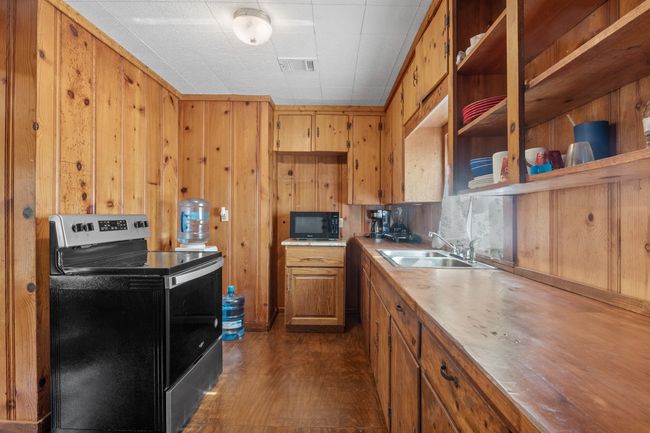 Kitchen featuring stainless steel electric stove, wood walls, sink, and dark wood-type flooring | Image 14