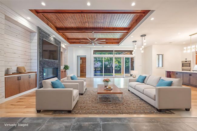 Living room with a fireplace, a wooden ceiling with exposed beams, recessed lighting, ceiling fan, and wooden walls | Image 4