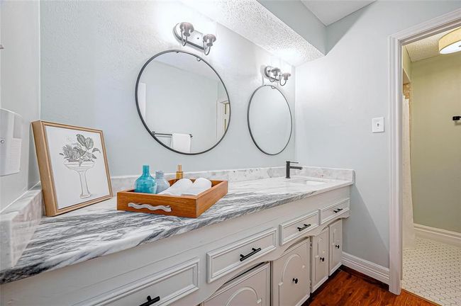 This bathroom features a dual-sink vanity with a quartzite countertop, modern fixtures and round mirrors. | Image 21