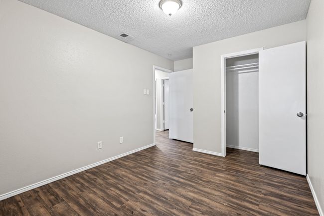 Unfurnished bedroom with dark wood-style floors, baseboards, a textured ceiling, and a closet | Image 16