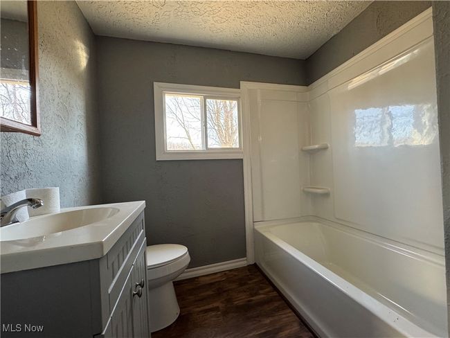 Bathroom featuring a textured wall, toilet, vanity, a textured ceiling, and wood finished floors | Image 11