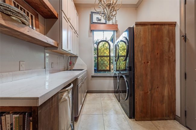 Washroom featuring light tile patterned floors, an inviting chandelier, cabinet space, a sink, and crown molding | Image 31