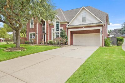 This is a two-story red brick home with large windows, an arched entryway, mature landscaping, and a prominent tree in the front yard. The property features a well-maintained lawn and a curved walkway leading to the front door. | Image 2