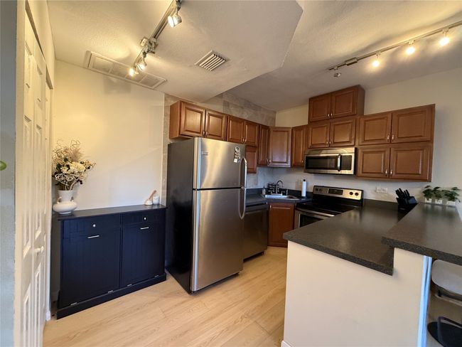 Kitchen featuring dark countertops, visible vents, appliances with stainless steel finishes, light wood-style floors, and a peninsula | Image 11