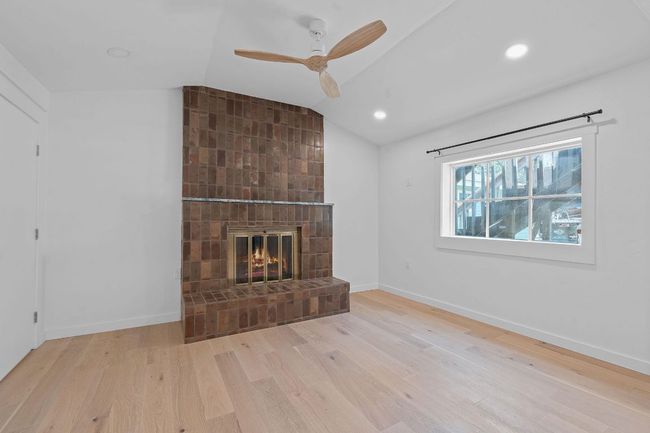 Unfurnished living room with wood finished floors, lofted ceiling, a ceiling fan, a brick fireplace, and recessed lighting | Image 5