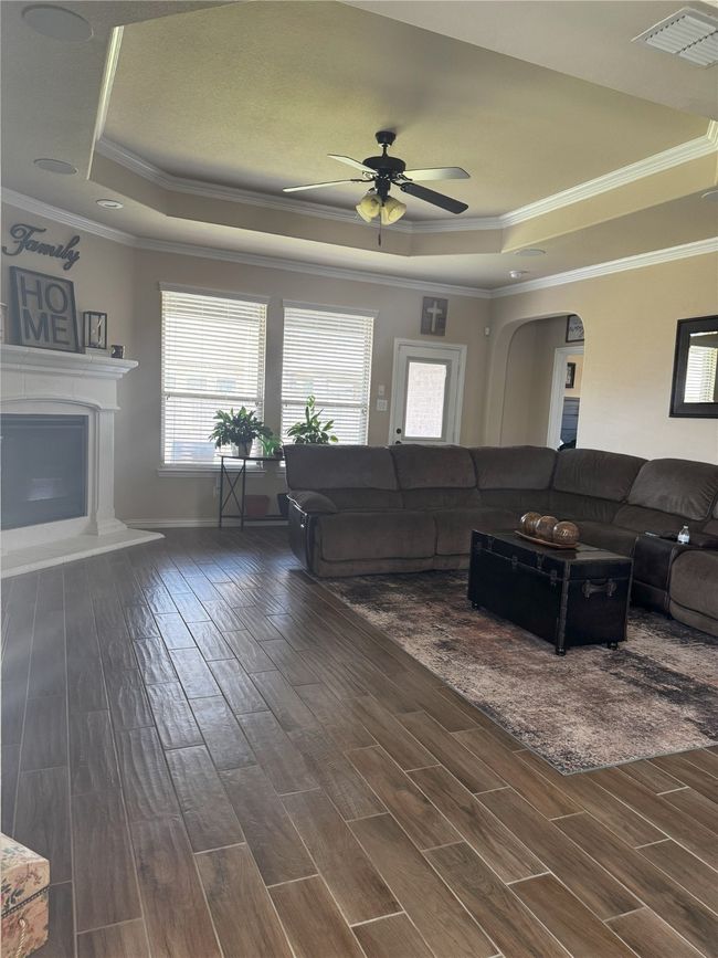 Living room with a raised ceiling, crown molding, wood finished floors, ceiling fan, and arched walkways and Fireplace | Image 23