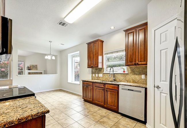 Kitchen with stainless steel dishwasher, decorative backsplash, light tile patterned floors, refrigerator, and a chandelier | Image 9