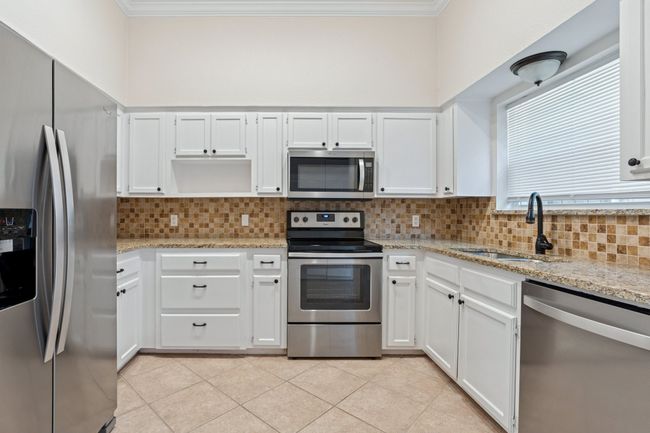 Kitchen with stainless steel appliances, ornamental molding, tasteful backsplash, light stone countertops, and white cabinetry | Image 12