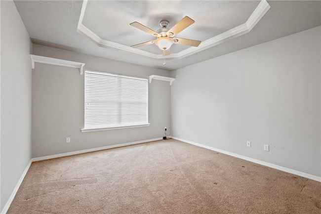 Carpeted empty room featuring a raised ceiling, ceiling fan, crown molding, and baseboards | Image 12