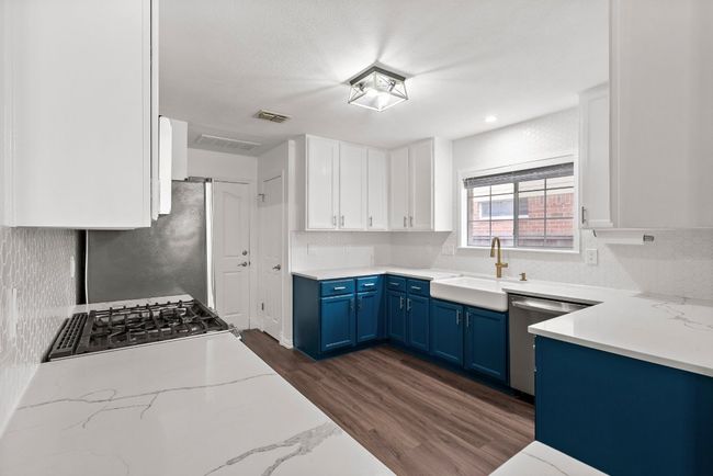 Kitchen featuring blue cabinetry, stainless steel appliances, a sink, backsplash, and light stone counters | Image 10