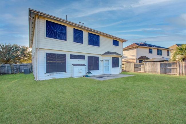 This two-story home features a spacious backyard with a well-maintained lawn, large windows, and a concrete patio area, perfect for outdoor activities and gatherings. The backyard is enclosed with a wooden fence, providing privacy and a secure environment. | Image 5