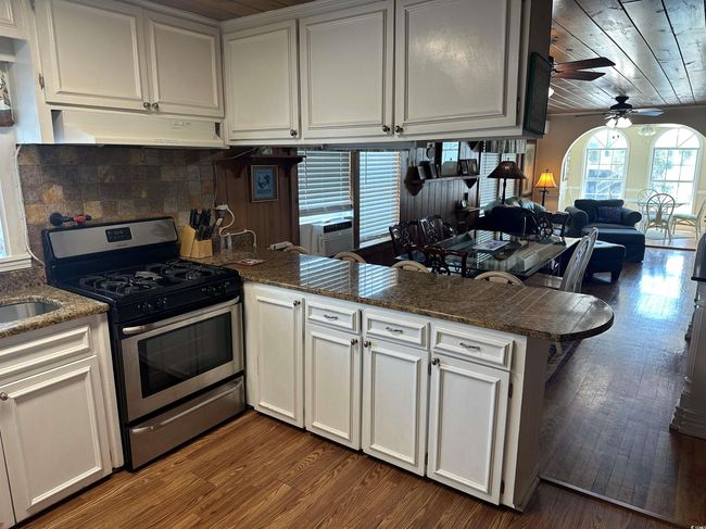 Kitchen featuring gas range, under cabinet range hood, a peninsula, ceiling fan, and dark wood-type flooring | Image 10
