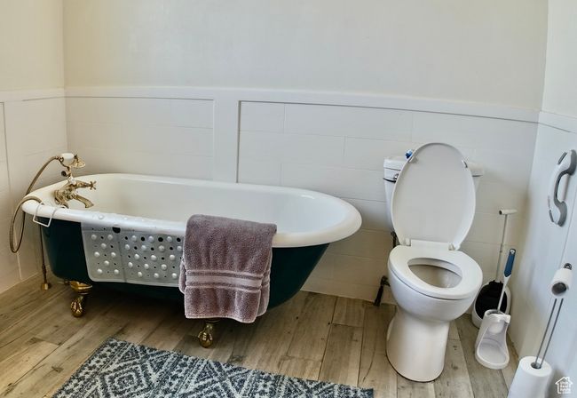 Bathroom featuring toilet, a freestanding tub, wainscoting, and wood finished floors | Image 40