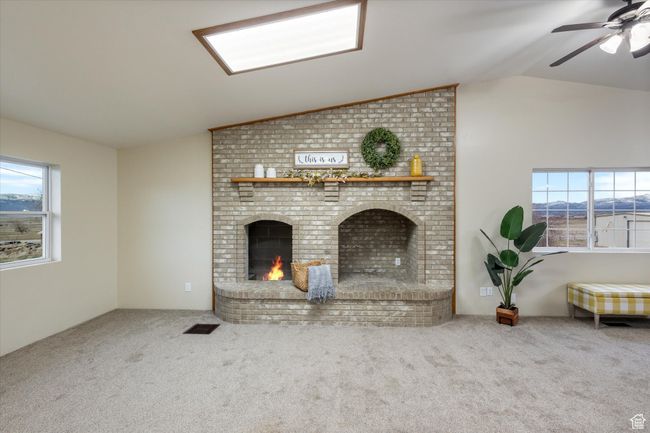 Unfurnished living room featuring a wealth of natural light, visible vents, carpet floors, lofted ceiling, and a brick fireplace | Image 10