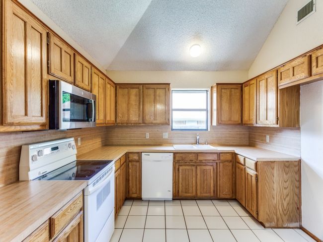 Kitchen with white appliances, vaulted ceiling, brown cabinets, backsplash, and light countertops | Image 14