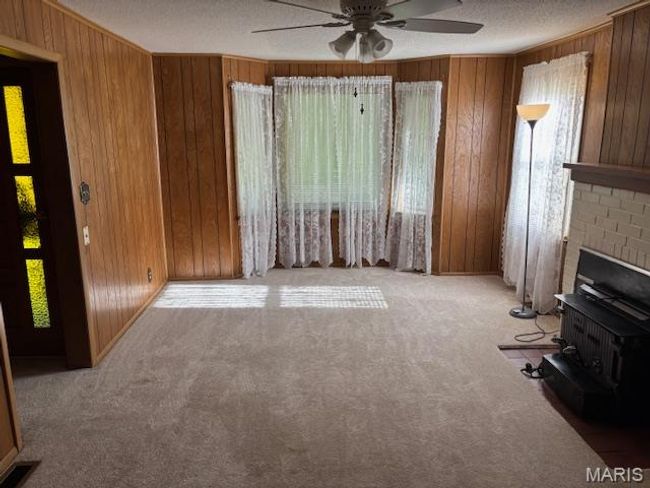 Unfurnished living room with plenty of natural light, wood walls, carpet, a ceiling fan, and a textured ceiling | Image 22