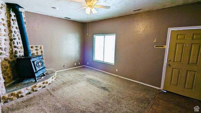 Unfurnished living room with a wood stove, ceiling fan, and dark colored carpet | Image 30