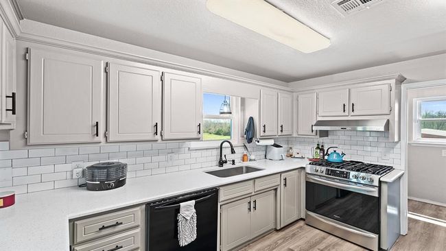 Kitchen featuring dishwasher, a sink, light wood-type flooring, under cabinet range hood, and stainless steel gas range oven | Image 38