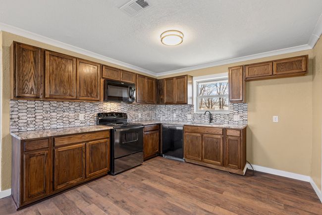 Kitchen with black appliances, dark wood-type flooring, a sink, and visible vents | Image 12
