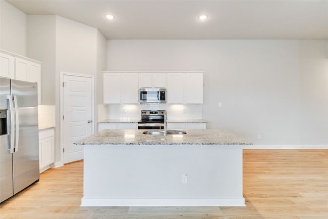 Kitchen featuring light wood-style floors, a kitchen island with sink, appliances with stainless steel finishes, and backsplash | Image 19
