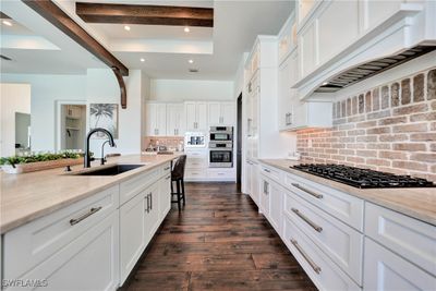 Kitchen featuring white cabinetry, custom range hood, gas stovetop, backsplash | Image 3