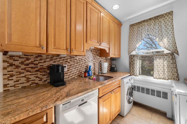Kitchen with radiator heating unit, dishwasher, a sink, light stone countertops, and washer / clothes dryer | Image 16