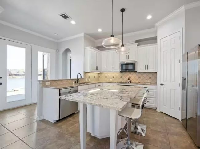 Kitchen featuring appliances with stainless steel finishes, crown molding, white cabinetry, tasteful backsplash, and a kitchen island | Image 7