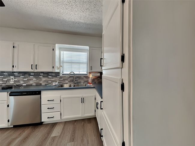 Kitchen with stainless steel dishwasher, dark countertops, a sink, white cabinets, and a textured ceiling | Image 6