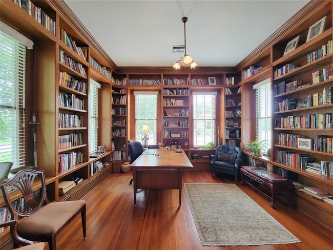 Discover a stunning front library featuring extensive solid wood bookshelves, elegant hardwood floors, and an antique chandelier, with pocket doors opening to the dining room. | Image 8