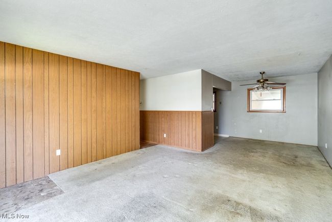 Carpeted empty room with wood walls, a ceiling fan, and a wainscoted wall | Image 11