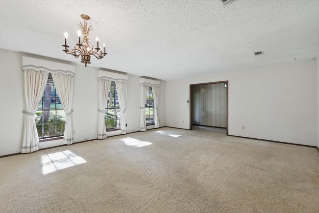Carpeted empty room featuring baseboards, visible vents, a textured ceiling, and a notable chandelier | Image 7