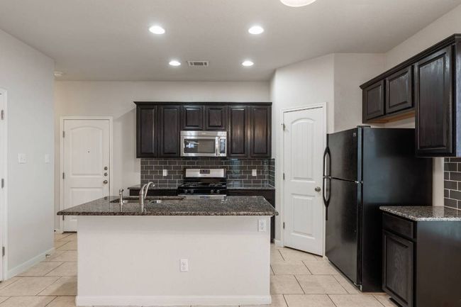 Kitchen features rich dark cabinetry, granite countertops, sleek stainless-steel and black appliances, including a refrigerator. | Image 17