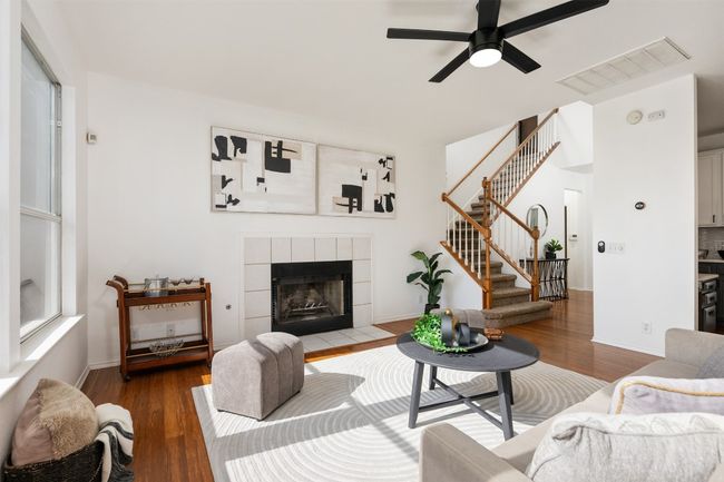 Living area with wood finished floors, a tiled fireplace, visible vents, and stairs | Image 6