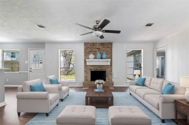 The generously sized family room features a fireplace as its focal point, framed by large windows that flood the space with natural light, and the beautiful wood-like flooring. | Image 5