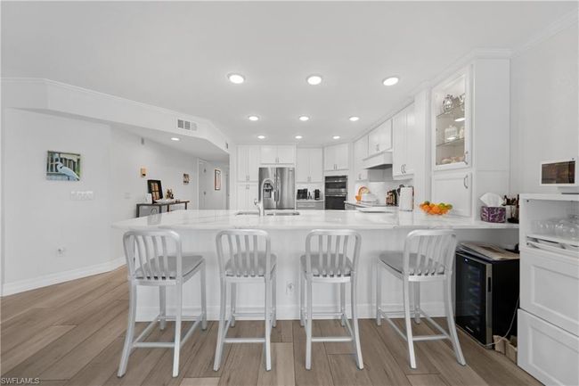 Kitchen featuring kitchen peninsula, appliances with stainless steel finishes, beverage cooler, light hardwood / wood-style flooring, and white cabinets | Image 10