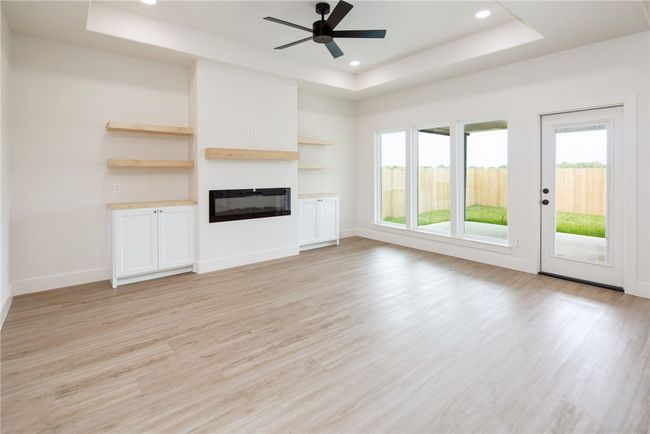 Unfurnished living room featuring a tray ceiling, light wood-style floors, a glass covered fireplace, a ceiling fan, and recessed lighting | Image 5