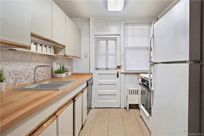 Kitchen featuring white fridge, tasteful backsplash, sink, stainless steel dishwasher, and white cabinets | Image 3