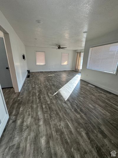 Unfurnished living room featuring a textured ceiling, dark hardwood / wood-style floors, and ceiling fan | Image 3