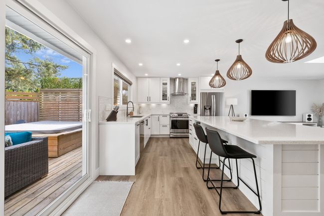Kitchen with light wood-type flooring, wall chimney range hood, backsplash, appliances with stainless steel finishes, and a sink | Image 8