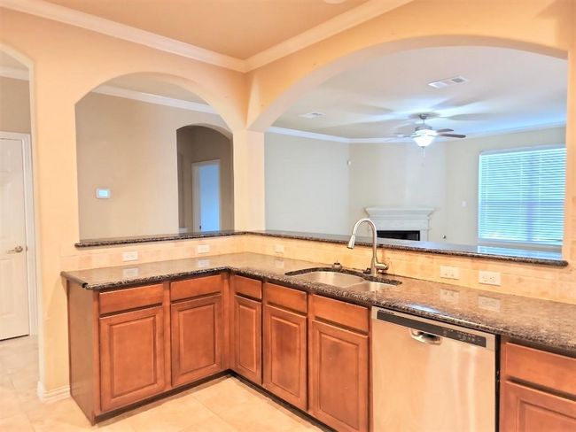 Kitchen featuring stainless steel dishwasher, a sink, dark stone countertops, a ceiling fan, and ornamental molding | Image 6