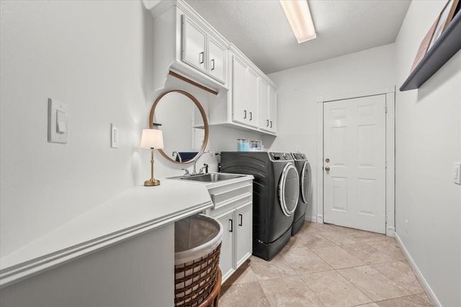 The laundry room brings charm and practicality with built-in cabinetry, sink, counter space, and an elegant round mirror to elevate the everyday. | Image 18