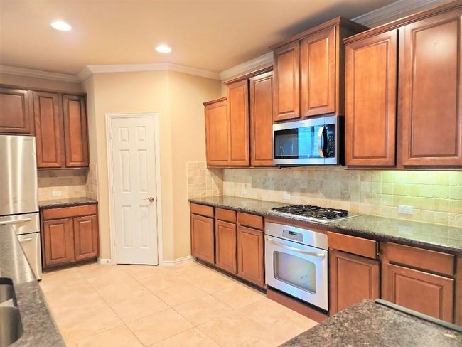 Kitchen featuring appliances with stainless steel finishes, tasteful backsplash, brown cabinets, crown molding, and light tile patterned flooring | Image 9