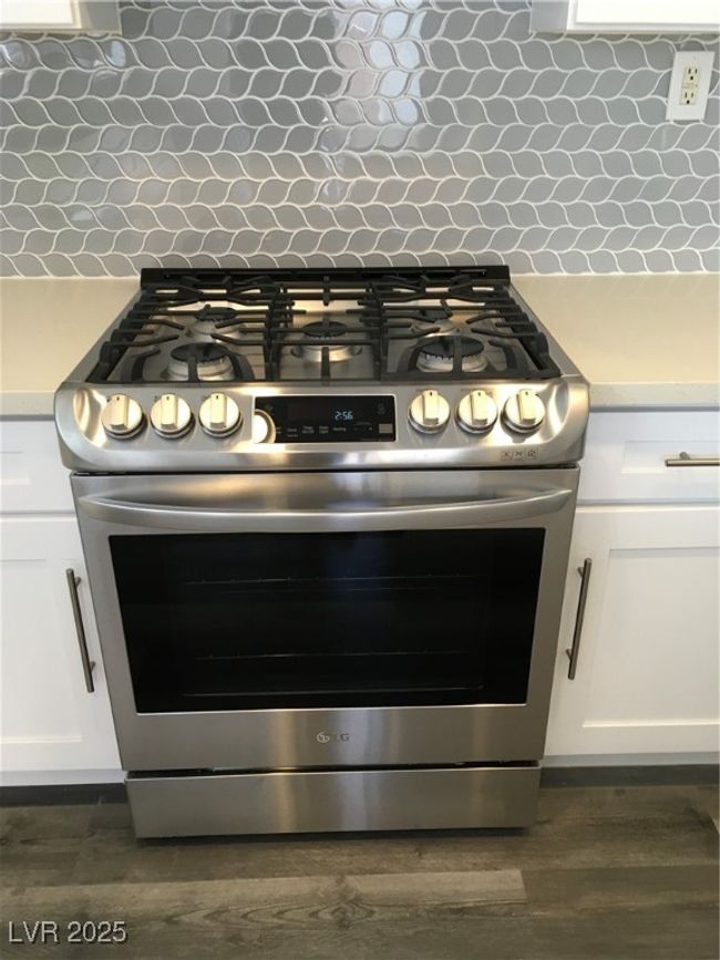 Room details with stainless steel gas range, dark wood-style flooring, decorative backsplash, light countertops, and white cabinets | Image 9